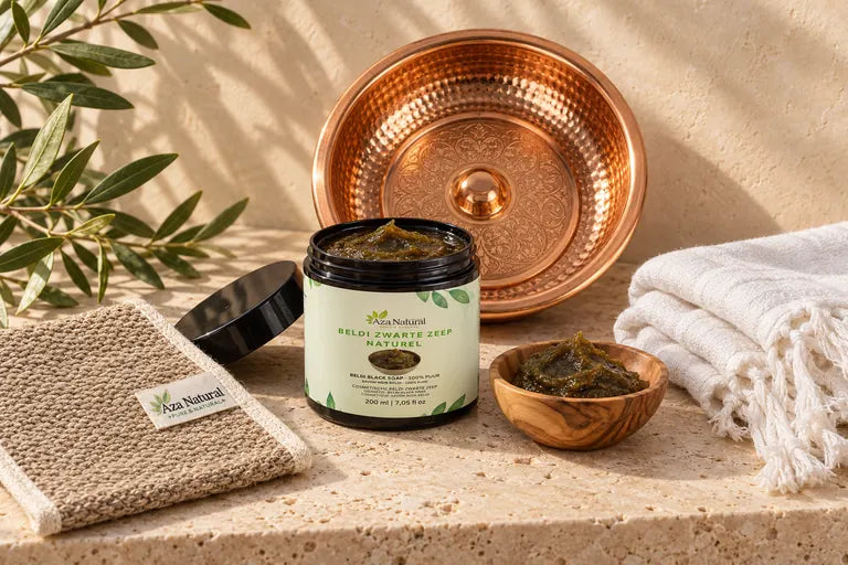 Beldi zwarte zeep naturel van Aza Natural met een scrubhandschoen, een hammamschaal en een handdoek op travertijn